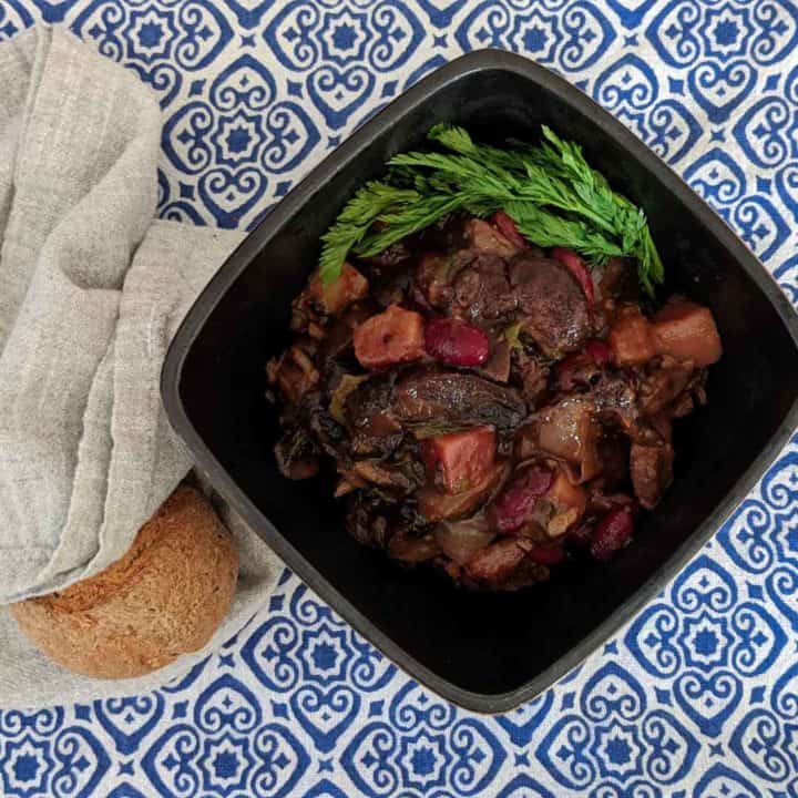 Photo of a bowl of mushroom stew on a blue and white tablecloth with a roll