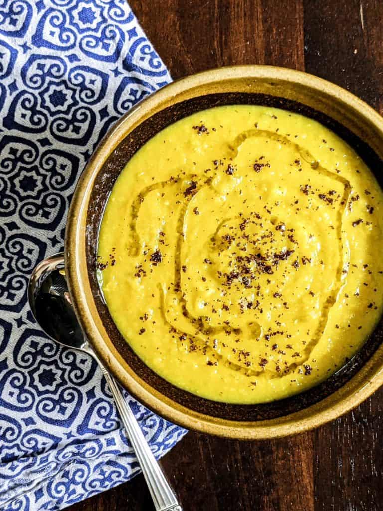 Overhead photo of a bowl of red lentil soup with a spoon on a blue and white cloth